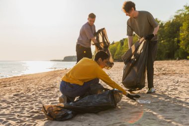 Dünya günü. Gönüllü eylemciler sahil bölgesindeki çöpleri topluyor. Kadınlar ve erkekler okyanus kıyısındaki çöp torbasına plastik çöp koyar. Çevre koruma kıyı bölgesi temizliği
