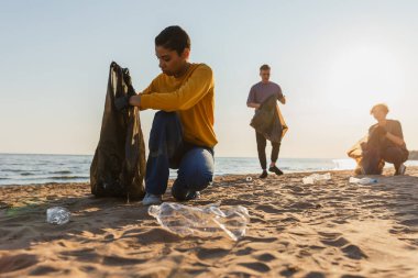Dünya günü. Gönüllü eylemciler, sahil bölgesindeki çöpleri topluyor. Kadınlar okyanus kıyısındaki çöp torbasına plastik çöp koyar. Çevre koruma kıyı bölgesi temizliği