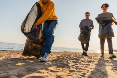 Dünya günü. Gönüllü eylemciler, sahil bölgesindeki çöpleri topluyor. Kadınlar okyanus kıyısındaki çöp torbasına plastik çöp koyar. Çevre koruma kıyı bölgesi temizliği