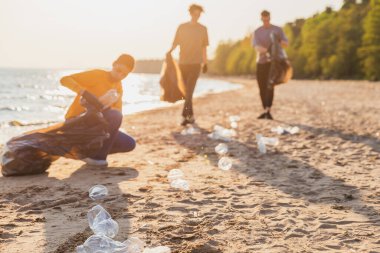 Dünya günü. Gönüllü eylemciler, sahil bölgesindeki çöpleri topluyor. Kadınlar okyanus kıyısındaki çöp torbasına plastik çöp koyar. Çevre koruma kıyı bölgesi temizliği
