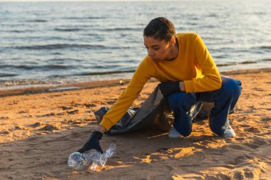 Dünya günü. Gönüllü eylemciler, sahil bölgesindeki çöpleri topluyor. Kadın, okyanus kıyısındaki çöp torbasına plastik çöp koyuyor. Çevre koruma kıyı bölgesi temizliği