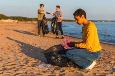 Dünya günü. Gönüllü eylemciler, sahil bölgesindeki çöpleri topluyor. Kadınlar okyanus kıyısındaki çöp torbasına plastik çöp koyar. Çevre koruma kıyı bölgesi temizliği