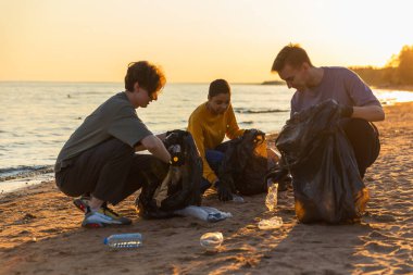 Dünya günü. Gönüllü eylemciler, sahil bölgesindeki çöpleri topluyor. Kadınlar okyanus kıyısındaki çöp torbasına plastik çöp koyar. Çevre koruma kıyı bölgesi temizliği