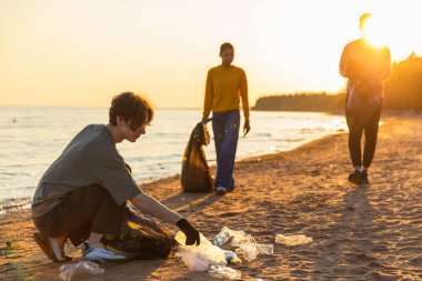 Dünya günü. Gönüllü eylemciler, sahil bölgesindeki çöpleri topluyor. Kadınlar okyanus kıyısındaki çöp torbasına plastik çöp koyar. Çevre koruma kıyı bölgesi temizliği