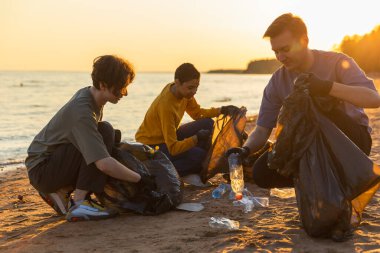 Dünya günü. Gönüllü eylemciler, sahil bölgesindeki çöpleri topluyor. Kadınlar okyanus kıyısındaki çöp torbasına plastik çöp koyar. Çevre koruma kıyı bölgesi temizliği