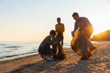 Dünya günü. Gönüllü eylemciler sahil bölgesindeki çöpleri topluyor. Kadınlar ve erkekler okyanus kıyısındaki çöp torbasına plastik çöp koyar. Çevre koruma kıyı bölgesi temizliği