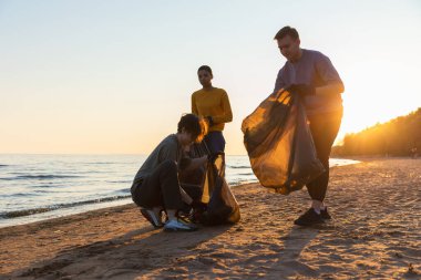 Dünya günü. Gönüllü eylemciler sahil bölgesindeki çöpleri topluyor. Kadınlar ve erkekler okyanus kıyısındaki çöp torbasına plastik çöp koyar. Çevre koruma kıyı bölgesi temizliği