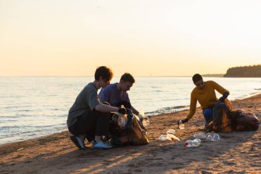 Dünya günü. Gönüllü eylemciler sahil bölgesindeki çöpleri topluyor. Kadınlar ve erkekler okyanus kıyısındaki çöp torbasına plastik çöp koyar. Çevre koruma kıyı bölgesi temizliği