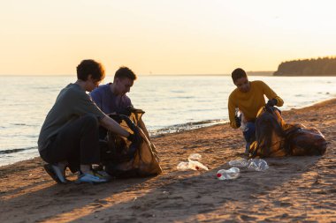 Dünya günü. Gönüllü eylemciler sahil bölgesindeki çöpleri topluyor. Kadınlar ve erkekler okyanus kıyısındaki çöp torbasına plastik çöp koyar. Çevre koruma kıyı bölgesi temizliği