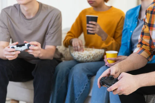 Home party. Group of friends playing video games at home, hands close up. Diverse group buddies having fun together indoor. Friendship leisure entertainment concept. Best friends enjoying weekend