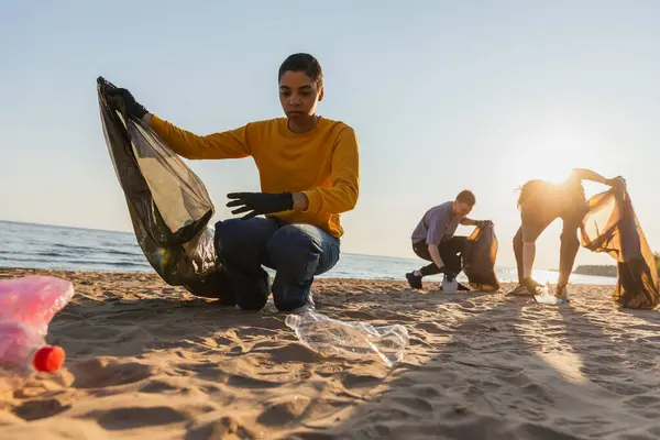 Earth day. Volunteers activists team collects garbage cleaning of beach coastal zone. Woman mans puts plastic trash in garbage bag on ocean shore. Environmental conservation coastal zone cleaning