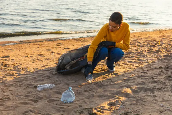 Earth day. Volunteers activists team collects garbage cleaning of beach coastal zone. Woman puts plastic trash in garbage bag on ocean shore. Environmental conservation coastal zone cleaning