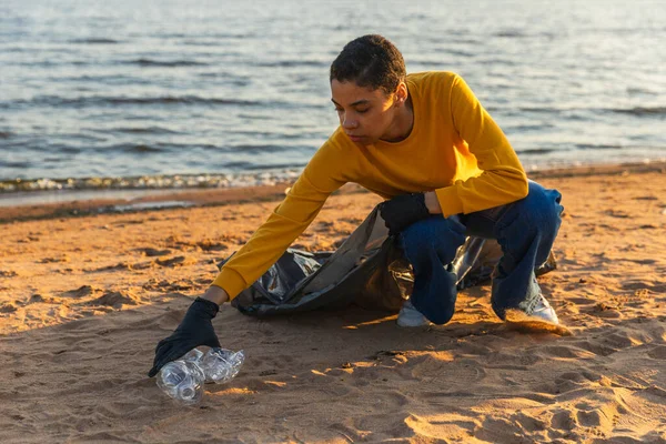 Earth day. Volunteers activists team collects garbage cleaning of beach coastal zone. Woman puts plastic trash in garbage bag on ocean shore. Environmental conservation coastal zone cleaning
