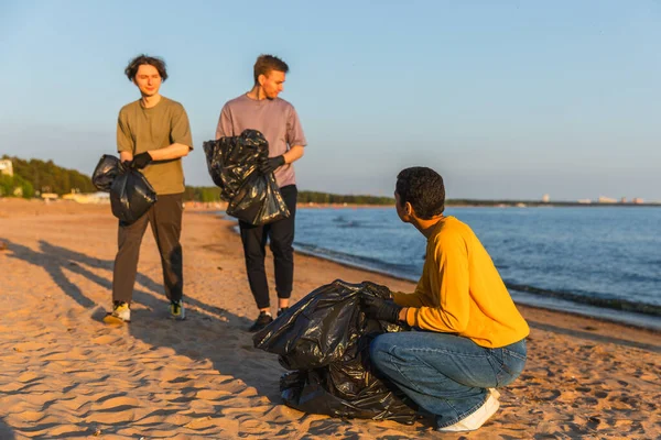 Earth day. Volunteers activists team collects garbage cleaning of beach coastal zone. Woman mans puts plastic trash in garbage bag on ocean shore. Environmental conservation coastal zone cleaning