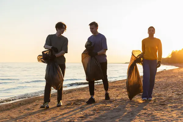 Earth day. Volunteers activists team collects garbage cleaning of beach coastal zone. Woman mans with trash in garbage bag on ocean shore. Environmental conservation coastal zone cleaning