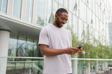 Afro-Amerikan bir adam elinde akıllı telefon, dokunmatik ekranlı parşömen kağıdı tutuyor. Şehir caddesinde. İnternette cep telefonu sörfü yapan bir adam sosyal medya uygulamaları kullanarak internetten alışveriş yapıyor. Cep telefonu bağımlılığı