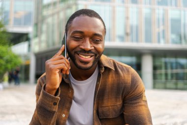 Açık havada, sokakta akıllı telefondan konuşan Afrikalı Amerikalı bir adam. Cep telefonlu bir adam arkadaşlarıyla sohbet ediyor. Gülümseyen kişi cep telefonuyla cevap veriyor. Cep telefonuyla konuşan adam