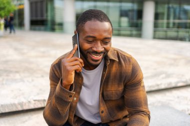 Açık havada, sokakta akıllı telefondan konuşan Afrikalı Amerikalı bir adam. Cep telefonlu bir adam arkadaşlarıyla sohbet ediyor. Gülümseyen kişi cep telefonuyla cevap veriyor. Cep telefonuyla konuşan adam