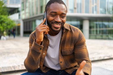 Açık havada, sokakta akıllı telefondan konuşan Afrikalı Amerikalı bir adam. Cep telefonlu bir adam arkadaşlarıyla sohbet ediyor. Gülümseyen kişi cep telefonuyla cevap veriyor. Cep telefonuyla konuşan adam