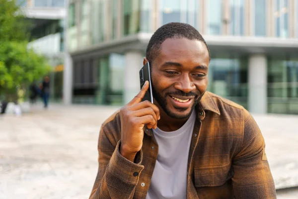 African american man talking on smartphone on street in city outdoor. Man with cell phone chatting with friends. Smiling person making answering call by cellphone. Guy having conversation by mobile