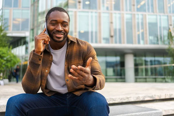 African american man talking on smartphone on street in city outdoor. Man with cell phone chatting with friends. Smiling person making answering call by cellphone. Guy having conversation by mobile