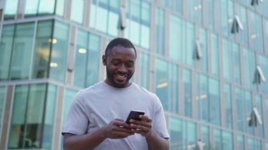 Afro-Amerikalı adam elinde akıllı telefon ekranı ile caddede daktilo yazıyor. Sosyal medya uygulamaları kullanarak internette cep telefonu sörfü yapan bir adam. İnternet üzerinden haber alışverişi cep telefonu bağımlılığı