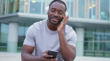 Müzik şarkısı konsepti. İyi bir başlangıç günü. Şehirde modern hit şarkıları dinleyen mutlu Afrikalı Amerikalı adam. Kulaklık takan adam telefonda en sevdiği müziği dinlemeyi sever. İnsanların yaşam tarzı neşesi