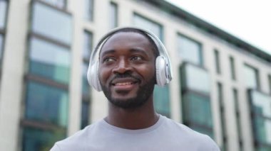 Müzik şarkısı konsepti. İyi bir başlangıç günü. Şehirde yürüyen modern hit şarkıları dinleyen mutlu Afrikalı Amerikalı adam. Kulaklık takan adam açık havada en sevdiği müziği dinlemeyi sever. Mutlu insanlar.