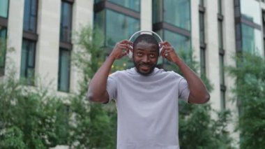 Müzik şarkısı konsepti. İyi bir başlangıç günü. Şehirde yürüyen modern hit şarkıları dinleyen mutlu Afrikalı Amerikalı adam. Kulaklık takan adam açık havada en sevdiği müziği dinlemeyi sever. Mutlu insanlar.
