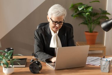 Confident stylish european middle aged senior woman using laptop at workplace. Stylish older mature 60s gray haired lady businesswoman sitting at office table. Boss leader teacher professional worker