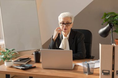 Confident stylish european middle aged senior woman using laptop at workplace. Stylish older mature 60s gray haired lady businesswoman sitting at office table. Boss leader teacher professional worker