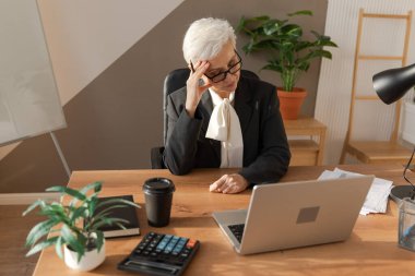 Ofiste stres yaşayan yaşlı bir kadın tapınaklara dokunuyor. Çalışmaktan yorgun düşmüş, baş ağrısı çeken şakakların alnına sürtünen olgun bir kadın. Uzun dizüstü bilgisayar görme sendromu. Ofis sendromu