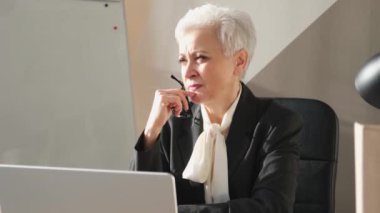İş yerinde dizüstü bilgisayar kullanan kendine güvenen Avrupalı orta yaşlı bir kadın. Modaya uygun, olgun 60 'ların beyaz saçlı iş kadını ofis masasında oturuyor. Patron öğretmen profesyonel işçi.