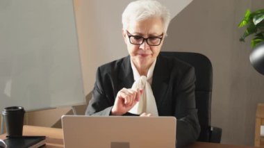 Confident stylish european middle aged senior woman using laptop at workplace. Stylish older mature 60s gray haired lady businesswoman sitting at office table. Boss leader teacher professional worker