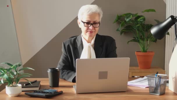 職場でラップトップを使用してスタイリッシュなヨーロッパの中年のシニア女性を自信を持って オフィスのテーブルに座ってスタイリッシュな古い成熟した60年代グレーの髪の女性実業家 上司指導教員 プロ労働者 — ストック動画