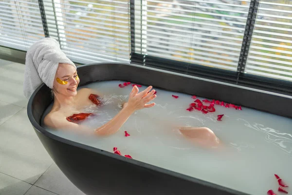 Spa relaxation. Woman lying in bath with red roses petals. Girl relaxing in bathroom at home. Pretty female enjoying taking hot bath. Stress relief. Rest after hard working day
