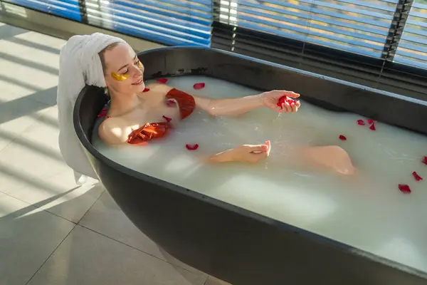 Spa relaxation. Woman lying in bath with red roses petals. Girl relaxing in bathroom at home. Pretty female enjoying taking hot bath. Stress relief. Rest after hard working day