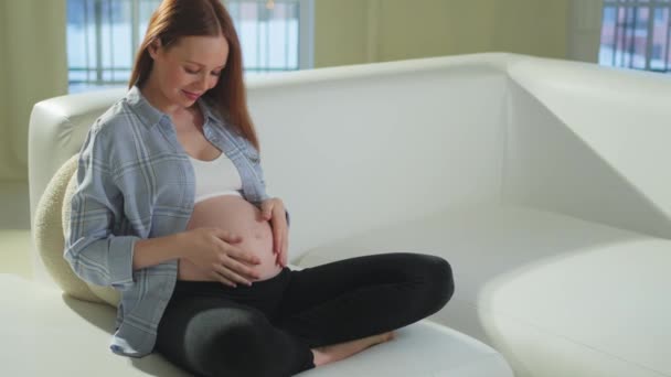 怀孕的母亲们期待着未来 怀孕妇女坐在家里的沙发上摸大肚子 女孩抱着她的肚子享受怀孕 母爱为人父母新生命的概念 — 图库视频影像