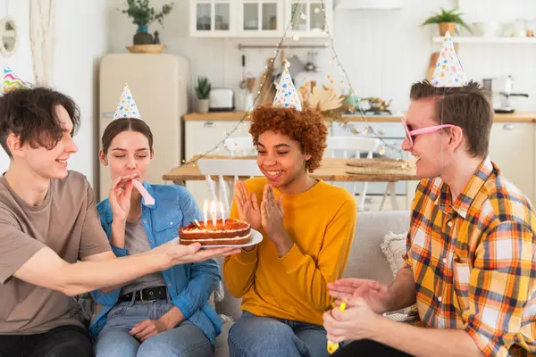 願い事をする 誕生日のケーキにろうそくを吹き飛ばすパーティーキャップを着ている女性 ハッピーバースデーパーティー 友人のグループは 少女の幸せな誕生日を願っています 自宅でパーティーで誕生日を祝う人 — ストック写真