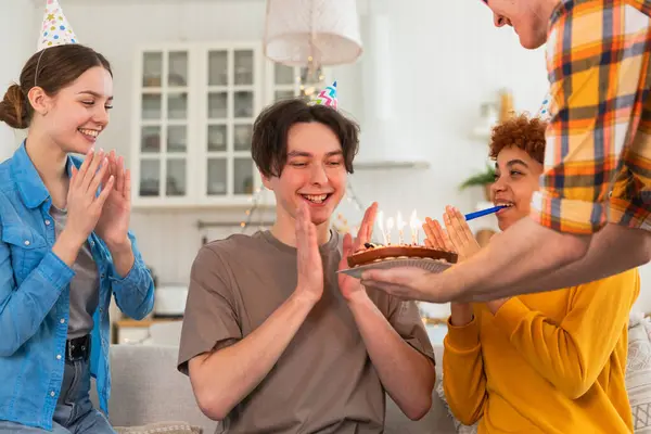 願い事をする 誕生日のケーキにろうそくを吹き飛ばすパーティーキャップを着ている男 ハッピーバースデーパーティー 友人のグループは幸せな誕生日を望んでいます 自宅でパーティーで誕生日を祝う人 — ストック写真