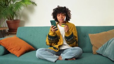 İnternetten alışveriş yapan Afrikalı Amerikalı bir kadın elinde akıllı telefonuyla altın kredi kartıyla ödeme yapıyor. Evde oturup internetten alışveriş yapan kız kredi kartı bilgilerini gir. Çevrimiçi alışveriş ekommerce dağıtım servisi