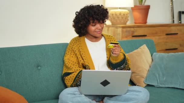 アフリカ系アメリカ人の女性は 金クレジットカードでオンラインで支払うラップトップショッピングを使用しています 女の子自宅でインターネット上で購入に座ってクレジットカードの詳細を入力します オンラインショッピングEc配信サービス — ストック動画