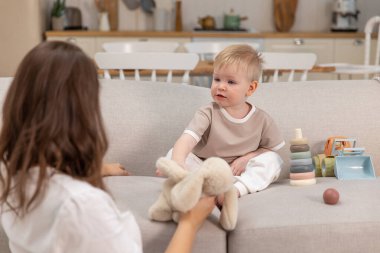 Evde mutlu bir aile. Anne ve bebek evdeki kanepede oyuncaklarla oynuyor. Küçük çocuk ve bebek bakıcısı birlikte eğleniyorlar. Genç kadın, anne, çocuk oturma odasında dinleniyor.