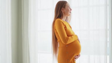 Hamilelik anneliği insanların gelecek beklentisi. Evinin penceresinin yanında koca göbekli hamile bir kadın var. Karnına sarılan ve hamileliğin tadını çıkaran bir kız. Annelik şefkati ebeveynlik yeni yaşam konsepti