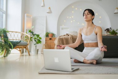 Yoga farkındalığı meditasyonu çevrimiçi. Evde dizüstü bilgisayar dersleriyle yoga yapan bir kadın. Lotus 'ta oturan kadın içeride meditasyon yapıyor. Nefes egzersizi yapan bir kız. Evde yoga.