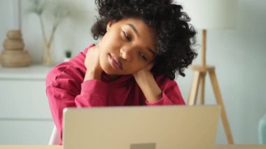Afro-Amerikalı bir kadın masada oturmuş, boynunu ovuşturuyor ve dizüstü bilgisayarla işe ara veriyor. Çok çalışan kız bilgisayarla uğraşmaktan yoruldu. Öğrenci iş kadını evde sıkılıyor.