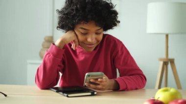 African girl holding smartphone touch screen typing scroll page at home. Woman with cell phone surfing internet using social media apps playing game. Shopping online Internet news cellphone addiction
