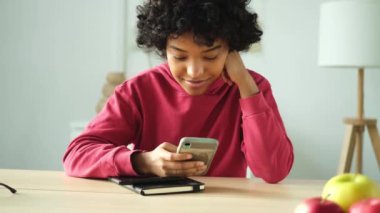 African girl holding smartphone touch screen typing scroll page at home. Woman with cell phone surfing internet using social media apps playing game. Shopping online Internet news cellphone addiction