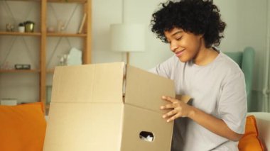 Paketleri açan Afrikalı kız kutuya bakıyor. Kutuyu açan mutlu kadın. Paket teslim edilen eşyalara bakan bir kadın. Tatmin olmuş istemci olumlu geri bildirim hızlı teslimatı