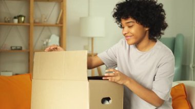 Paketleri açan Afrikalı kız kutuya bakıyor. Kutuyu açan mutlu kadın. Paket teslim edilen eşyalara bakan bir kadın. Tatmin olmuş istemci olumlu geri bildirim hızlı teslimatı